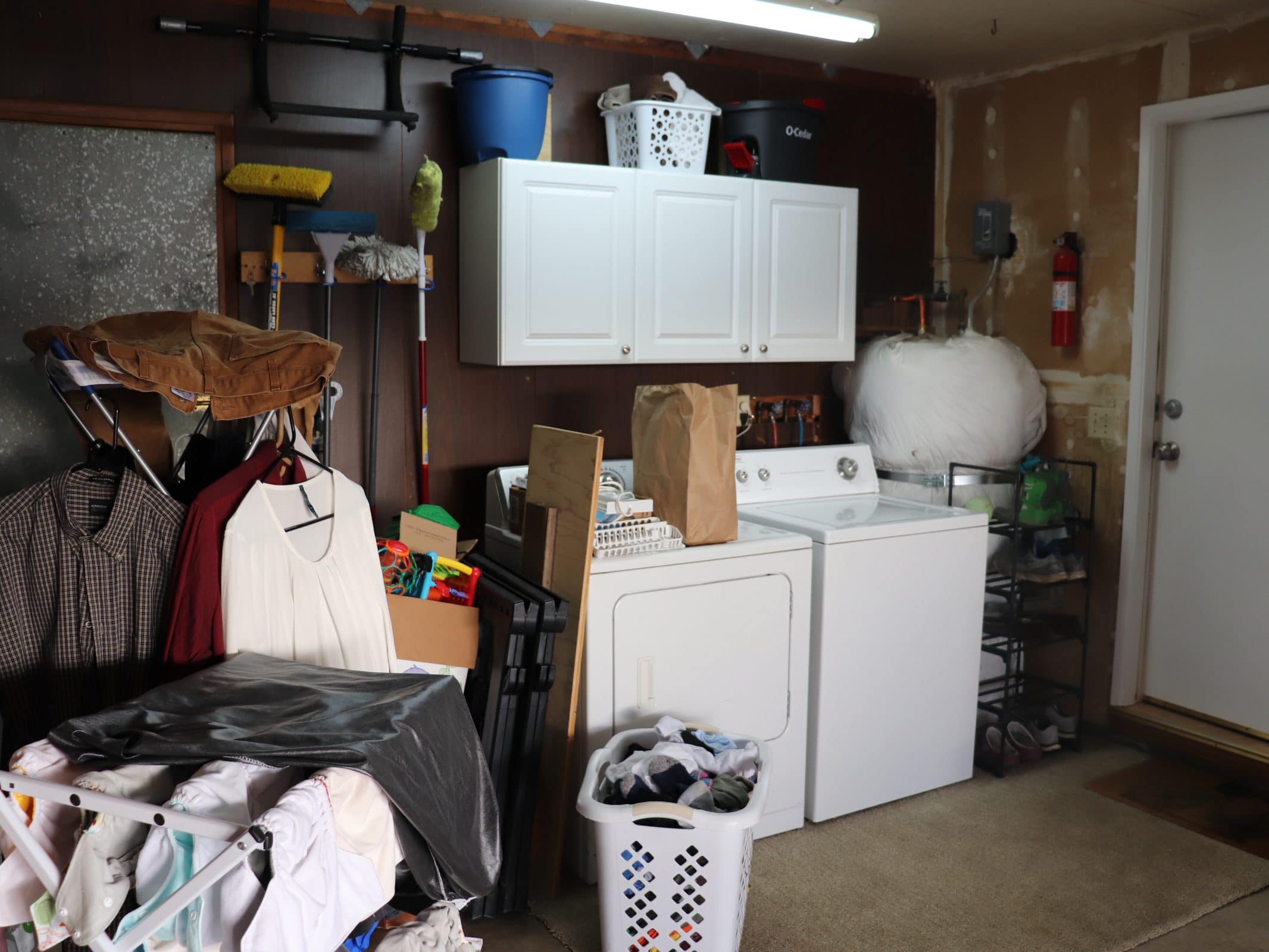 cluttered garage laundry room with hung laundry, a white washer and dryer, white cabinets, a water heater, a blue bucket, a white basket and a black mop bucket