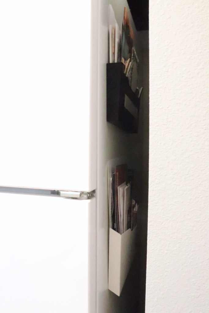 A white refrigerator with two magnetic organizer pockets stuck on the side with papers in them, one white and one black 