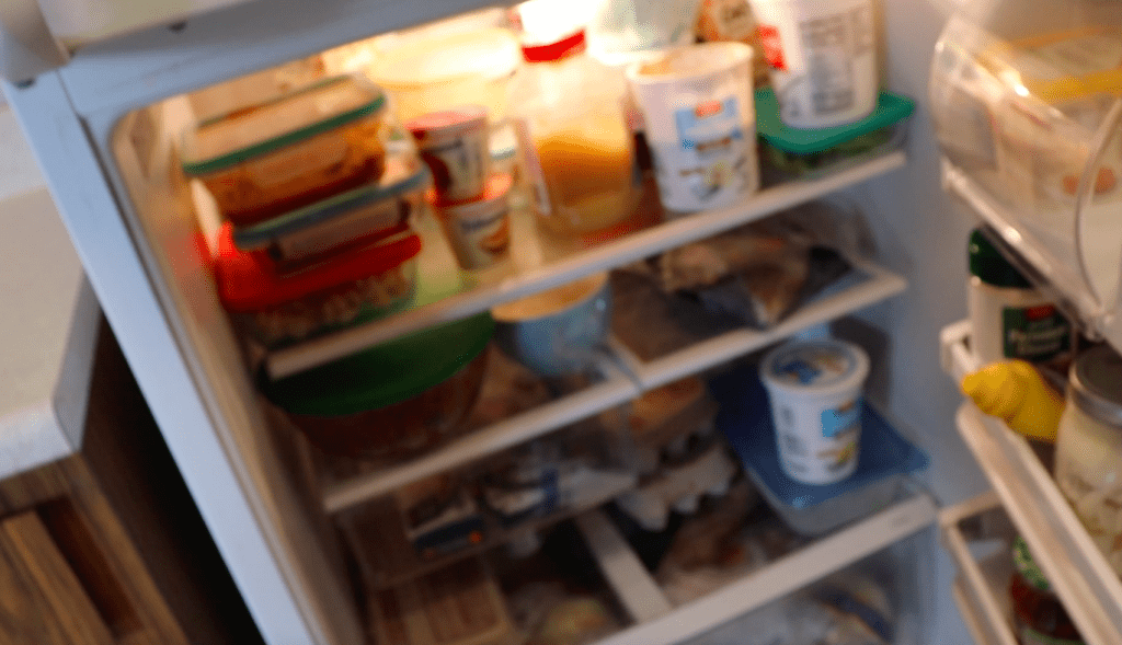 Blurry photo of an open white fridge cluttered with a bunch of food containers inside