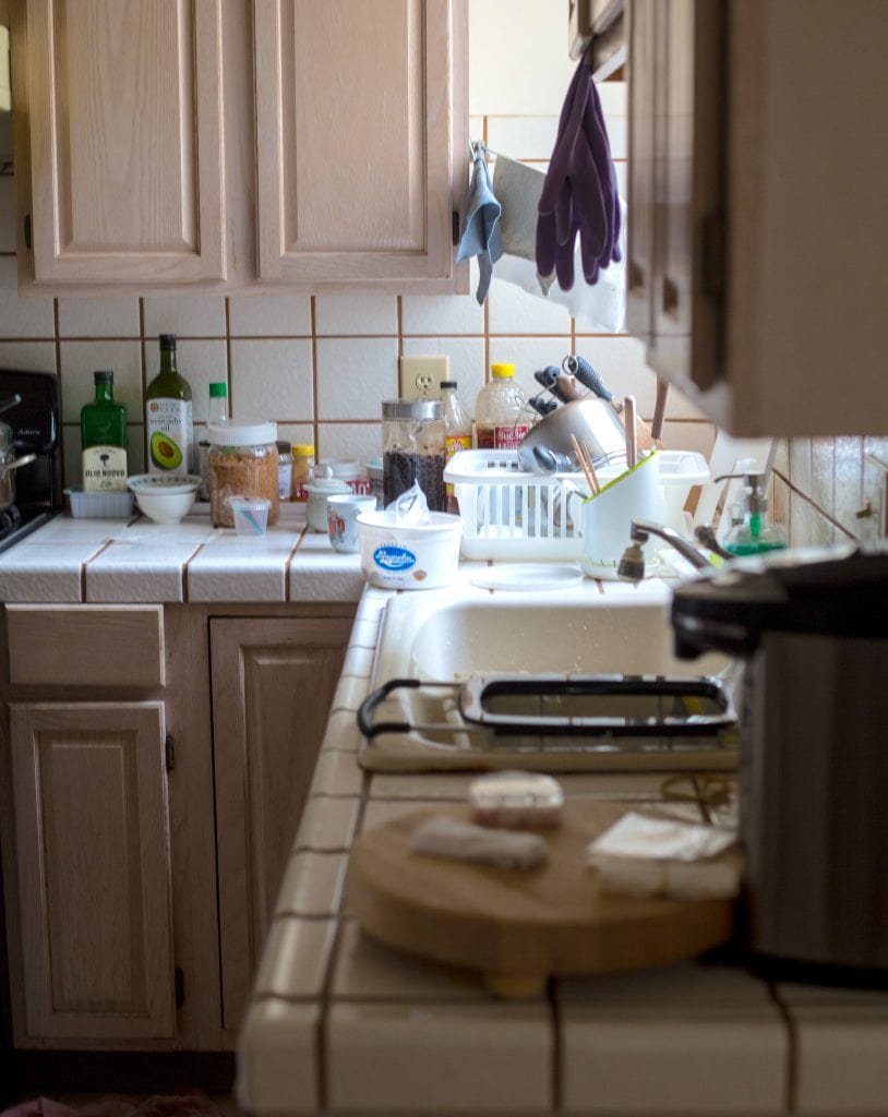 A white tiled kitchen counter filled with clutter and dirty dishes